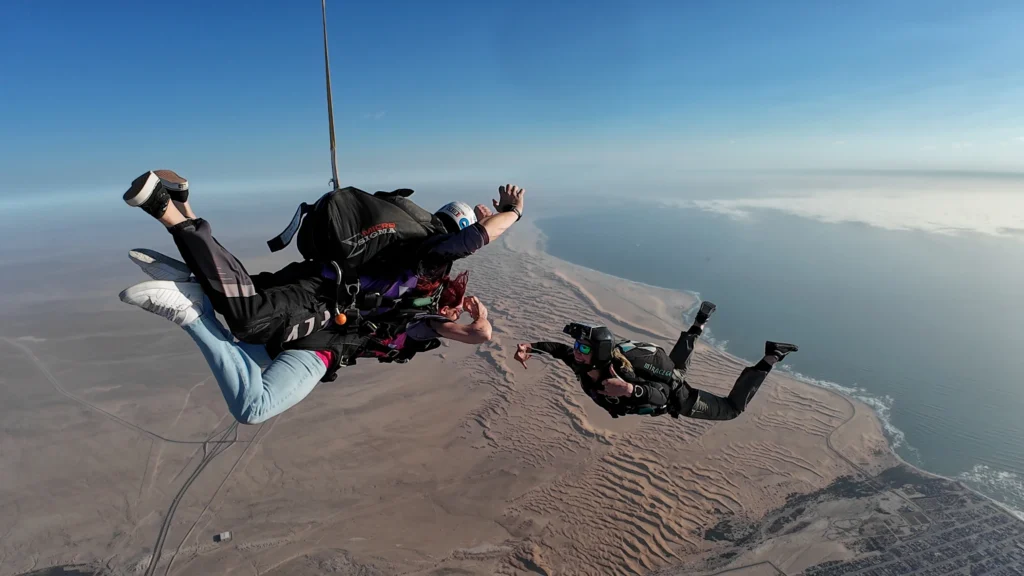 Tandem pair and camera flyer freefall together above the coastal dunes, skydive Namibia coast