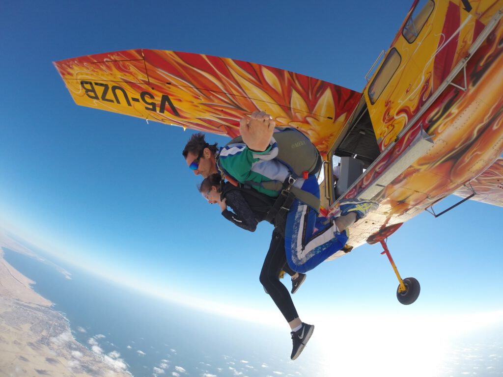 Tandem skydivers dangle from the biplane wing during a skydive Namibia coast exit