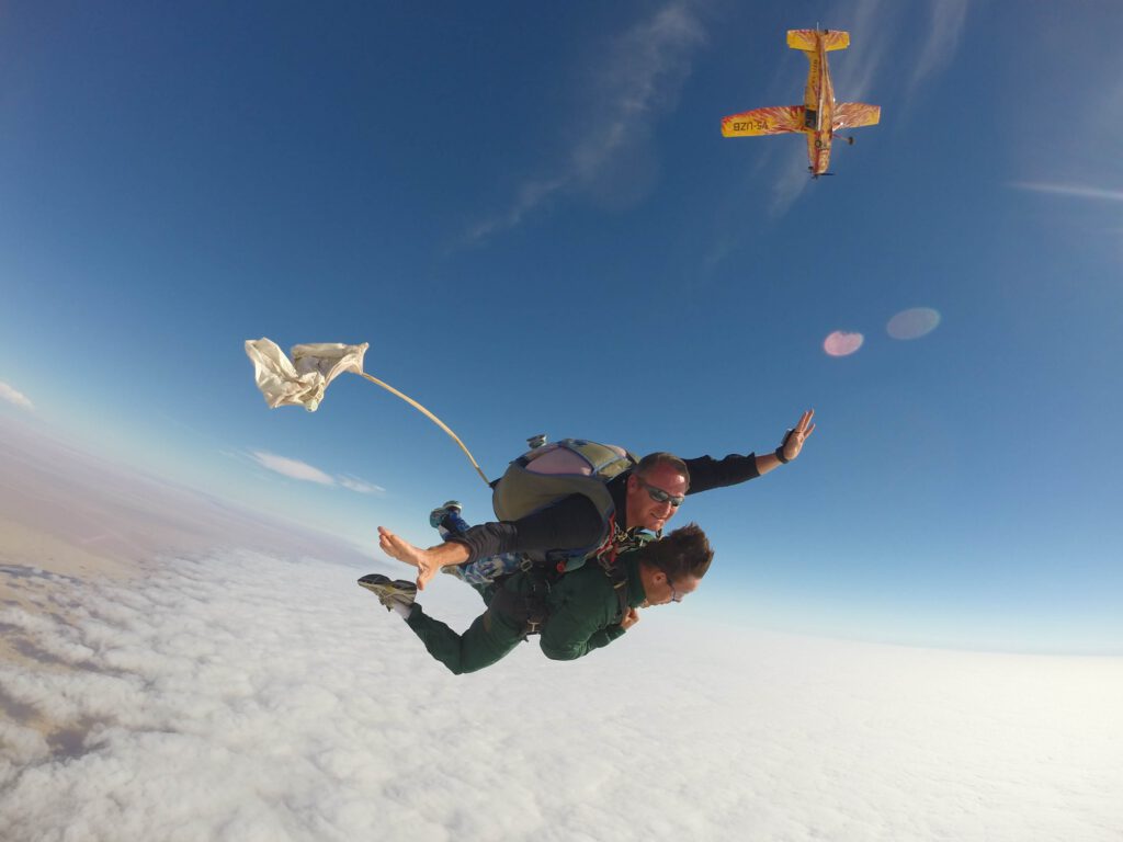 Tandem skydivers in freefall beside a yellow biplane above the Atlantic coast skydive zone