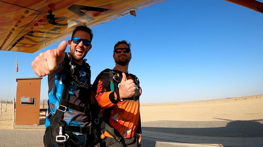 Tandem instructor and passenger pose for skydiving Namibia thumbs up at the airfield