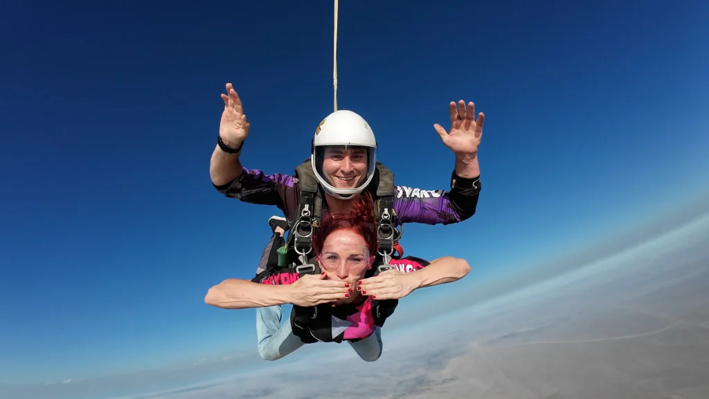 Tandem passenger blows a kiss to the camera in freefall beside her instructor above Swakopmund