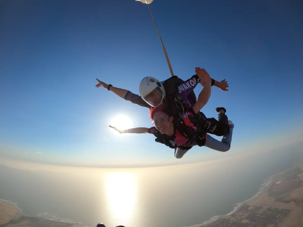 Smiling tandem skydivers freefalling over Swakopmund with sun and ocean behind