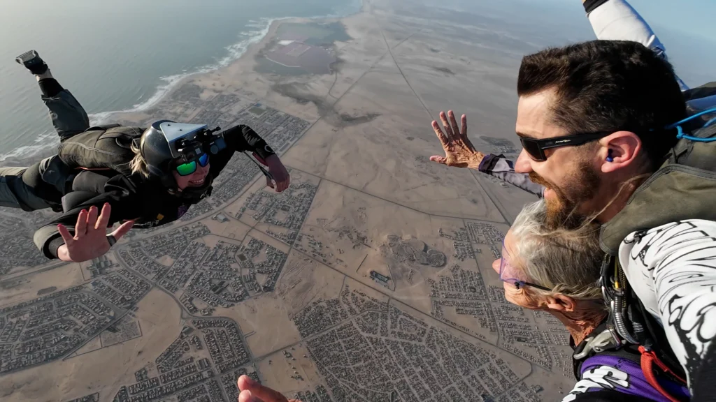Tandem pair in freefall beside a camera flyer high above Swakopmund and the Atlantic coast