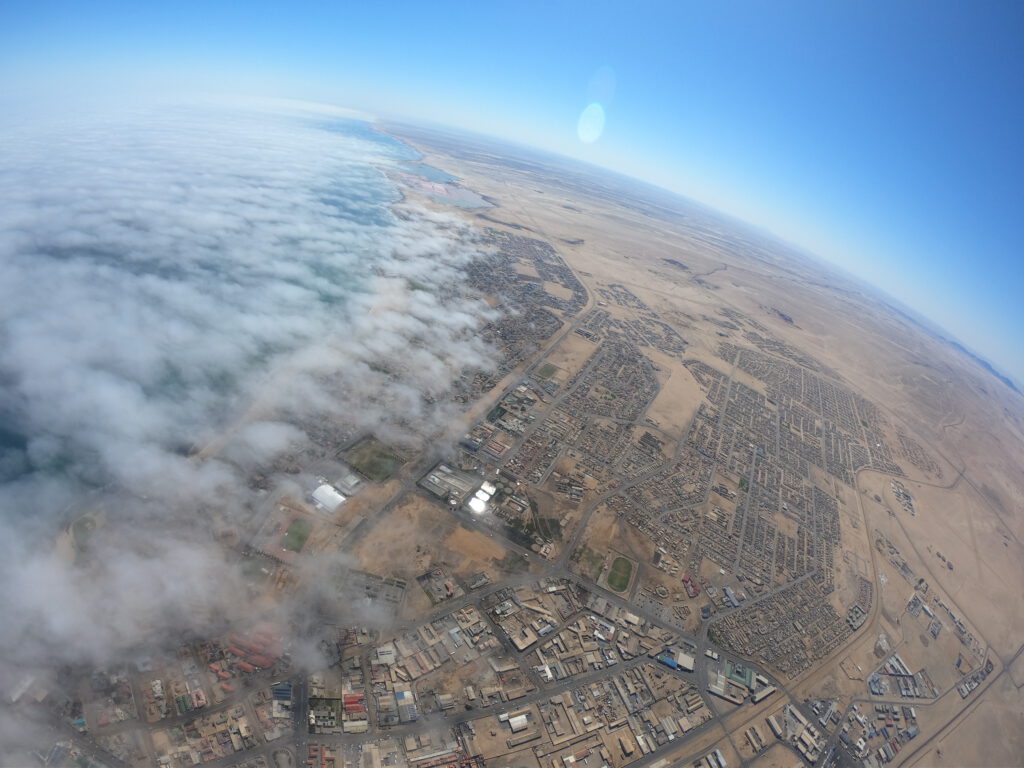 Fisheye aerial view of a foggy coastline and desert town, skydive Namibia coast