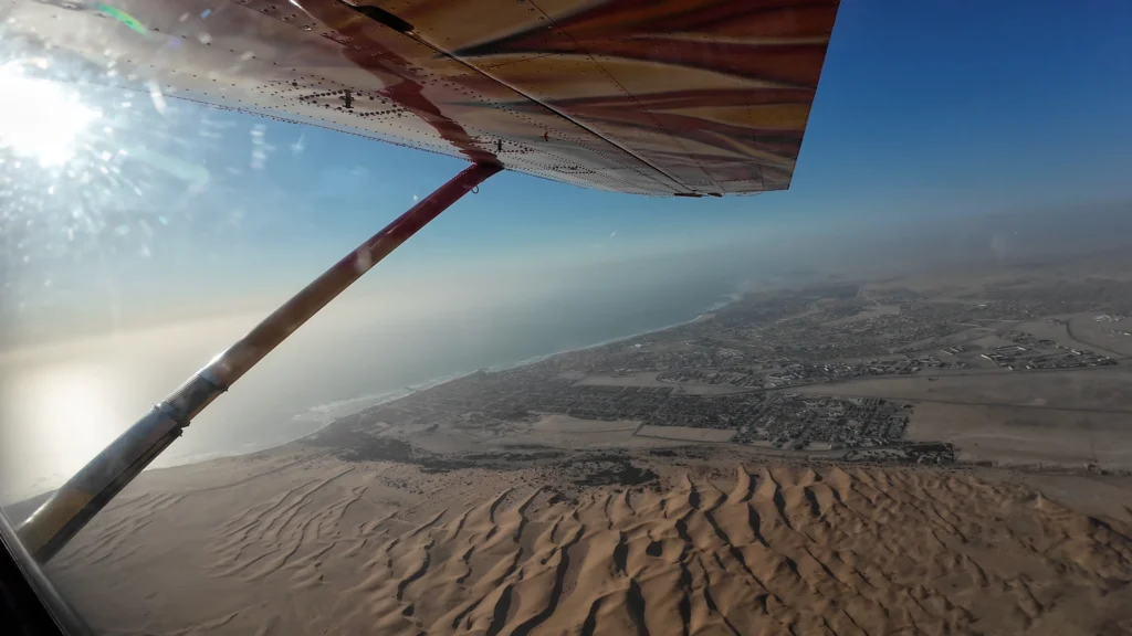 View beneath the plane's wing over sweeping Swakopmund dunes and coastline