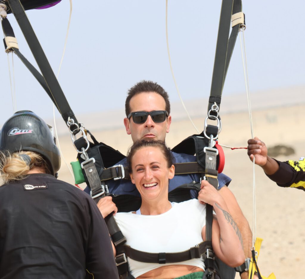 Beaming tandem passenger stays clipped to her instructor as crew help with the harness after landing