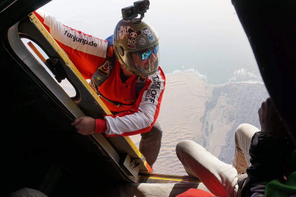 Camera flyer leans from the aircraft door above dunes on an Atlantic coast skydive