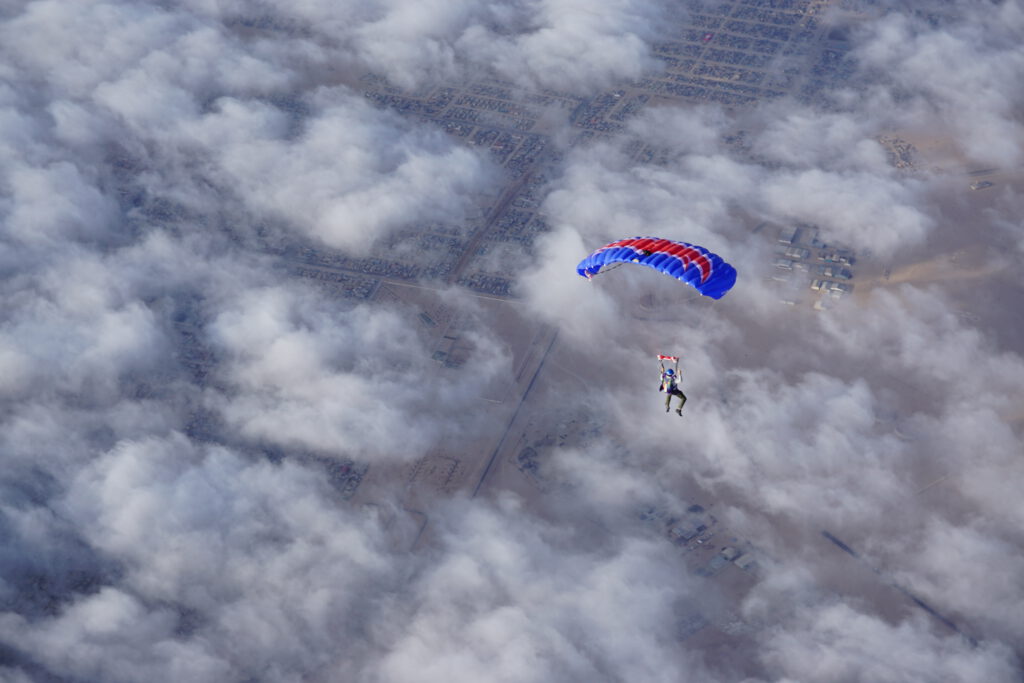 Skydiver glides under a blue and red canopy through the clouds