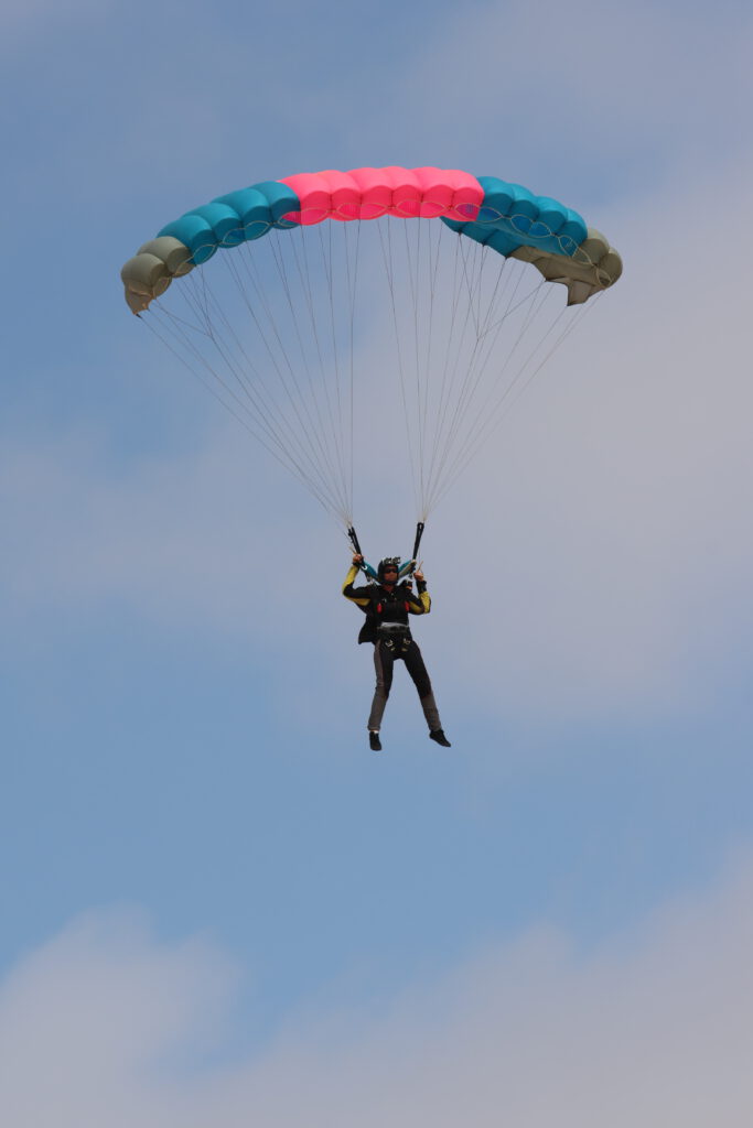 Skydiver flies a teal and pink canopy high in the sky, skydiving Namibia