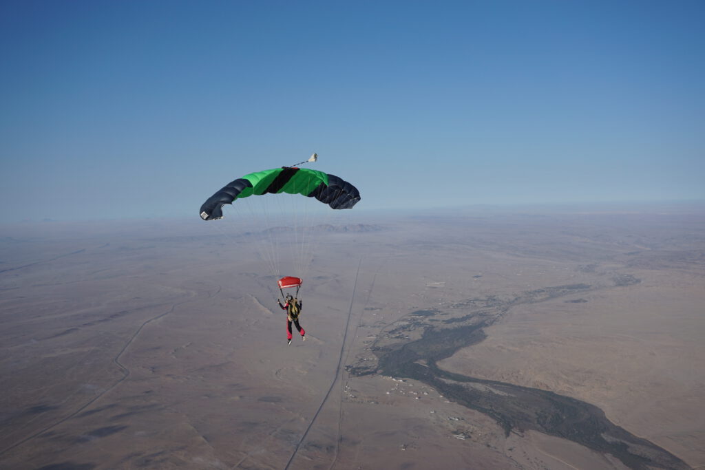 Skydiver flies a green and black canopy above the open desert, skydiving Namibia