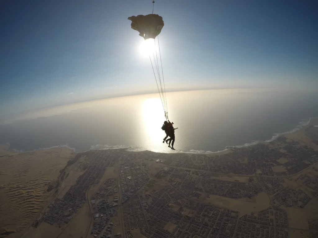 Tandem canopy silhouette drifts above sunlit ocean on a skydive Namibia coast descent