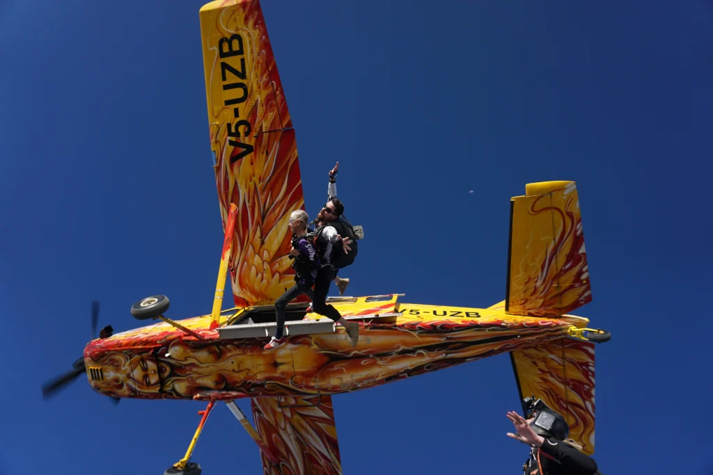 Tandem pair leaps from the flame-painted Angel to begin their skydive Swakopmund jump