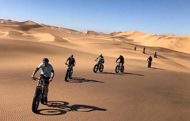 Cyclists riding fat bikes across the Swakopmund dunes at sunrise