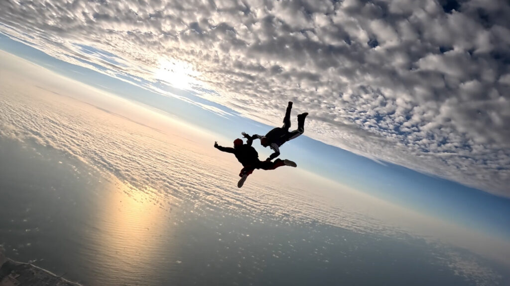 Instructor holds an AFF student in freefall silhouetted against a sunset over the Atlantic near Swakopmund