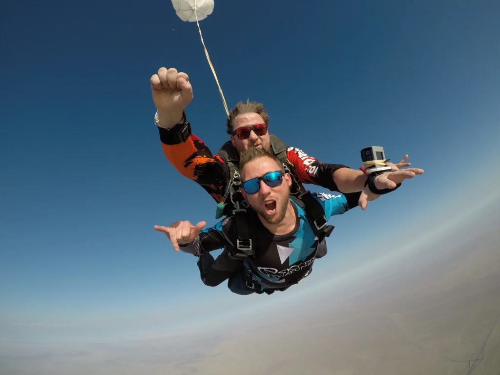 Tandem pair freefalls with GoPro in hand high above the coast, Atlantic coast skydive
