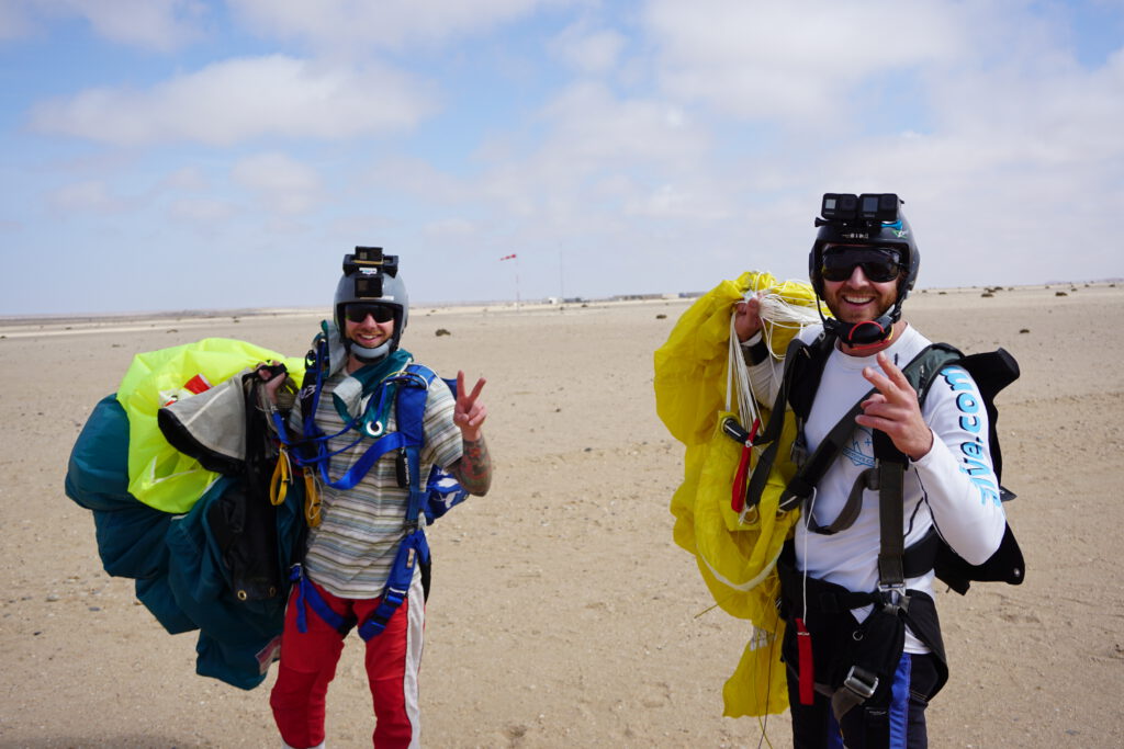Two jumpers carry folded yellow canopies across the desert airfield, skydiving Namibia