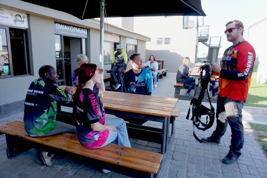 Instructor explains the tandem harness to guests during an outdoor safety briefing, skydiving Namibia