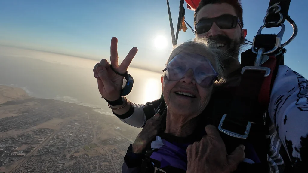 Senior passenger and instructor flashes a peace sign mid-air during an Atlantic coast skydive