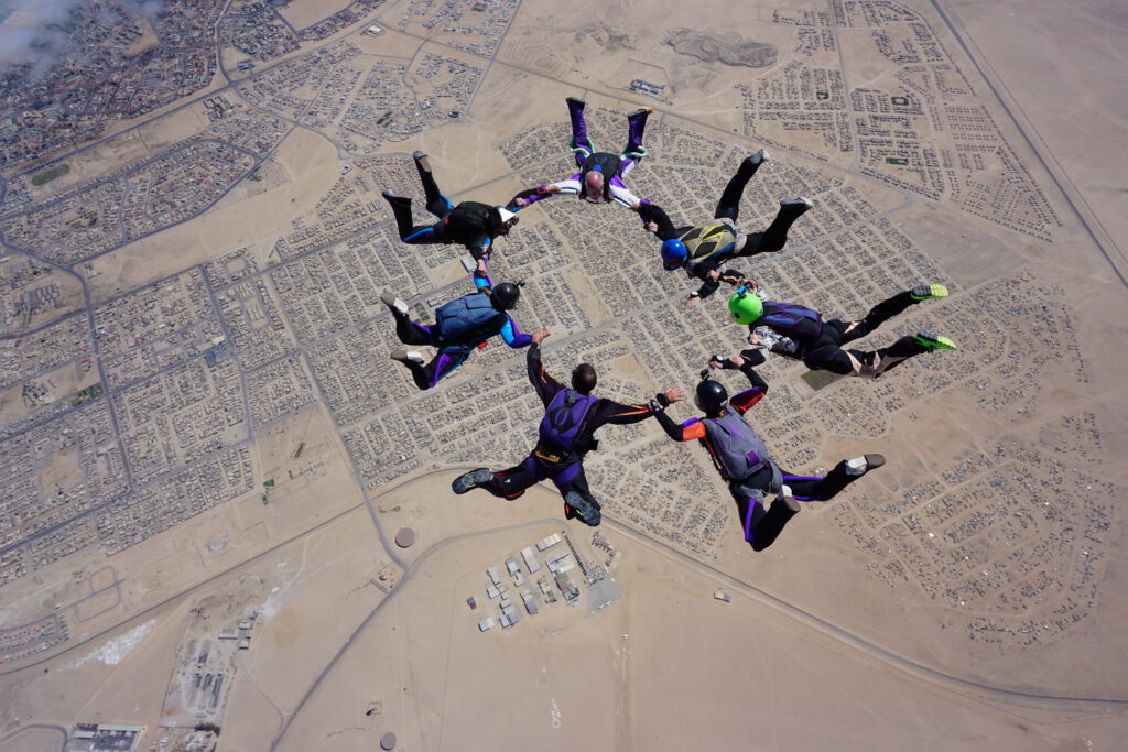 Seven skydivers link hands in a skydiving Swakopmund formation jump above town