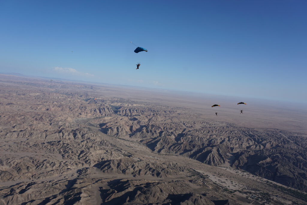 Skydivers glide under open parachutes above the Moon Landscape during skydiving Namibia