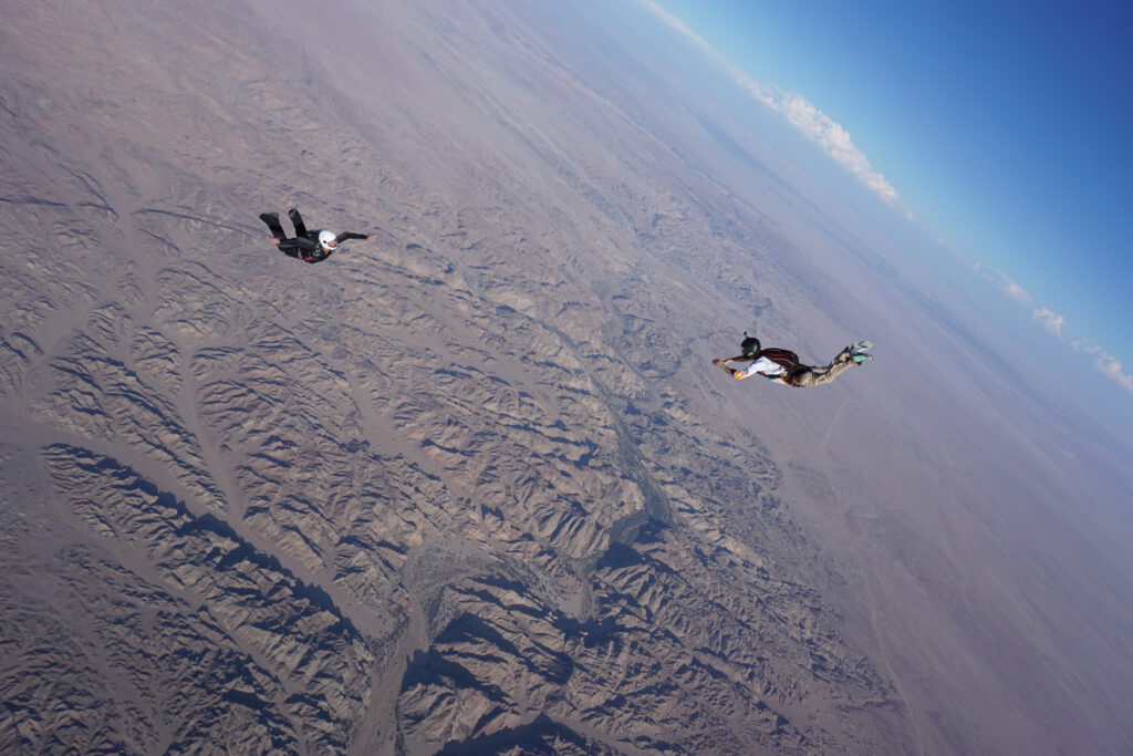 Two skydivers track side by side above the Moon Landscape