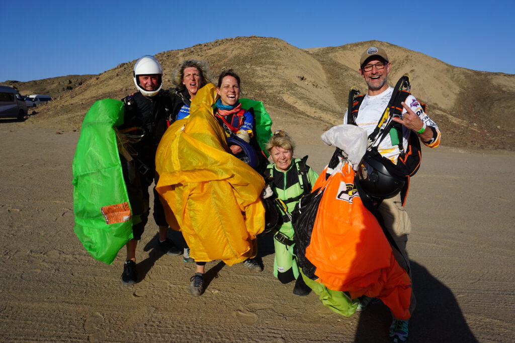 Cheerful skydivers carry colorful canopies across the Swakopmund dunes after landing