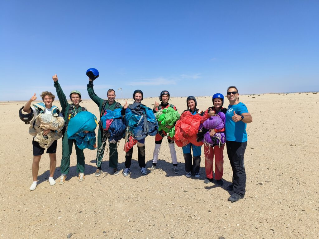 Skydiving group poses with packed parachutes across the Swakopmund dunes