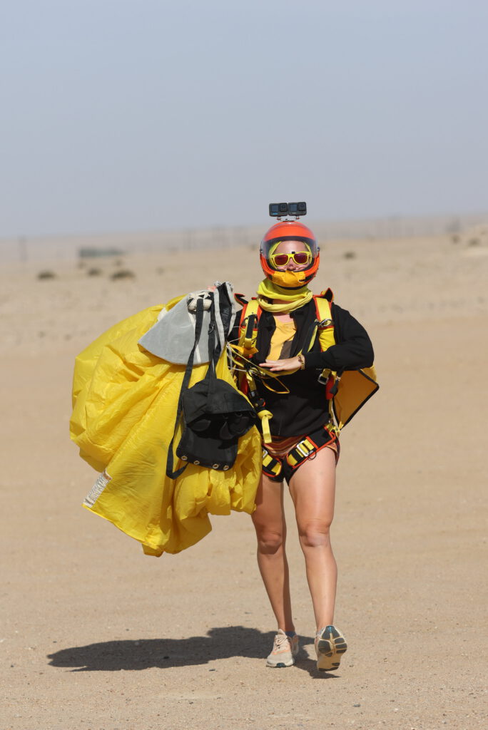 Tandem skydiving instructor walking across the desert after landing with yellow canopy in Namibia