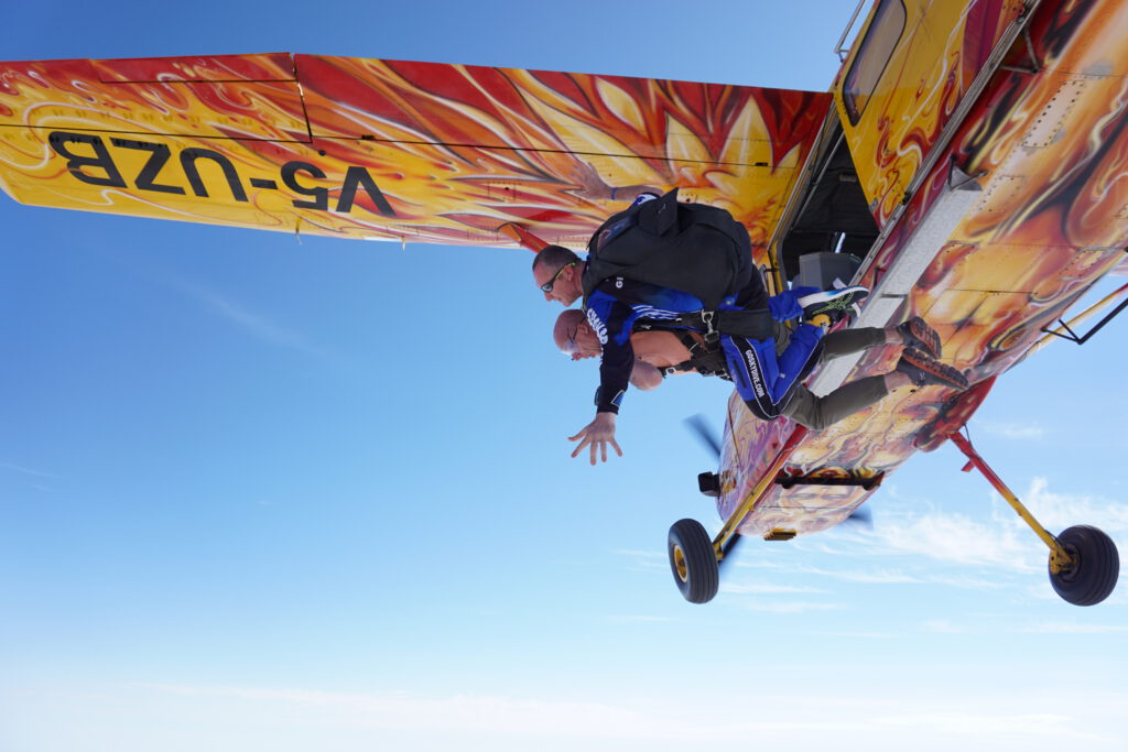 Tandem instructor and passenger exit a flame-painted plane during a tandem skydive Swakopmund