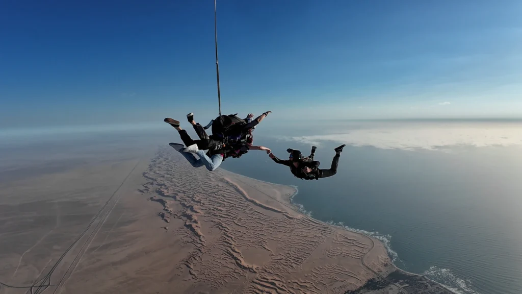 Tandem instructor and passenger skydiving in freefall over Swakopmund coastline with cameraflyer capturing the jump