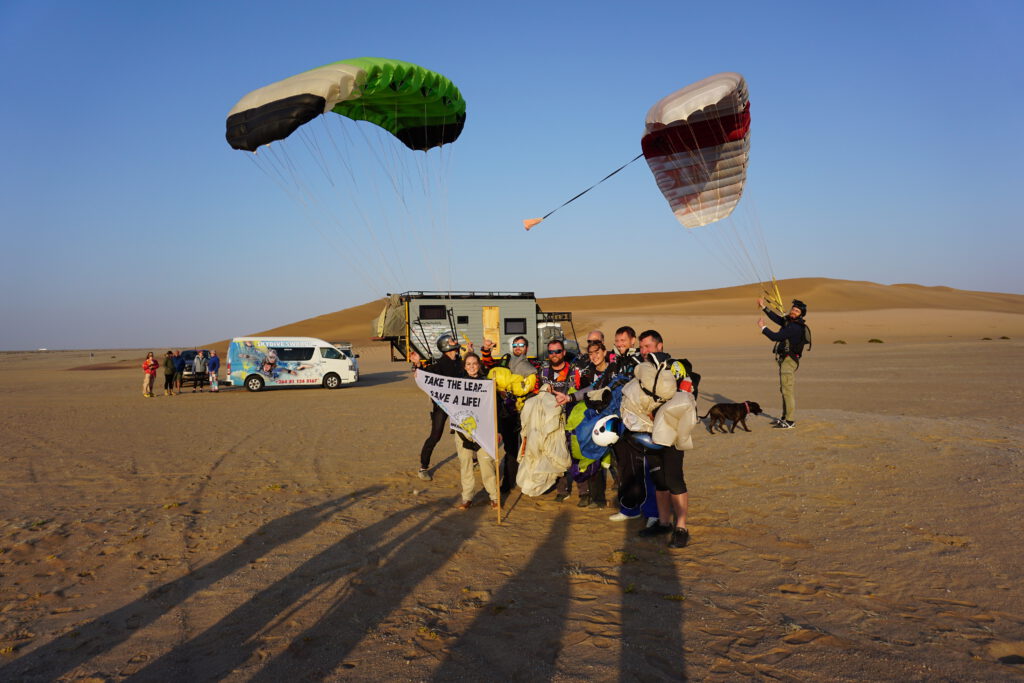 Skydiving team celebrates a landing among the Swakopmund dunes at sunset