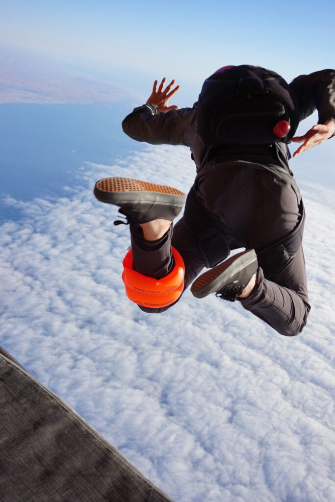 Skydiver exits the aircraft into freefall above the clouds and coastline near Swakopmund