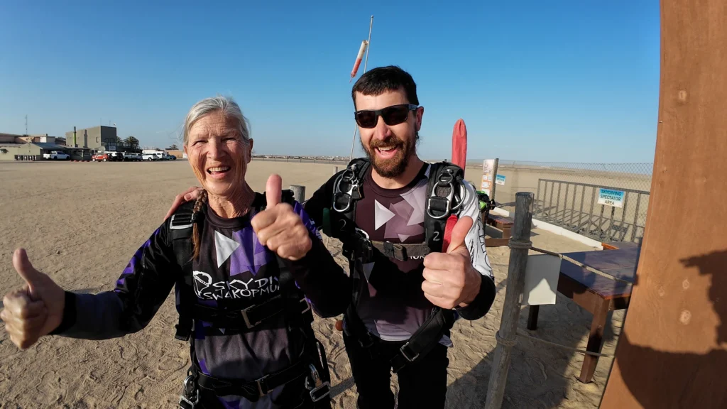 Elderly passenger and instructor give thumbs up at the Swakopmund dropzone before their tandem skydive