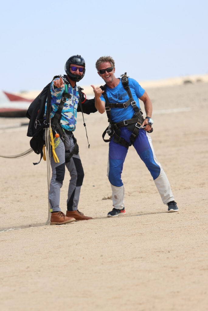 Two solo skydivers pose and give a shaka on the desert airfield after landing near Swakopmund